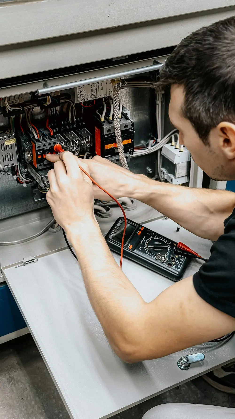 Electrician testing wire connections in electrical control panel with multimeter